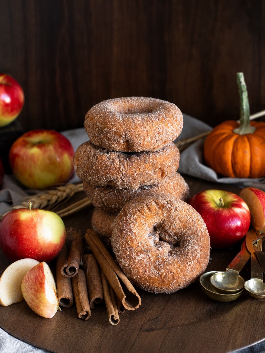 Sugar-coated apple cider donuts styled with apples, cinnamon, and a small pumpkin